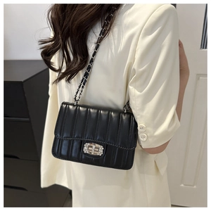 Detail of black quilted chain bag with crystal-embellished twist lock on white blazer
