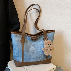 Blue denim tote bag with brown leather trim and a cute plush bear charm for daily use