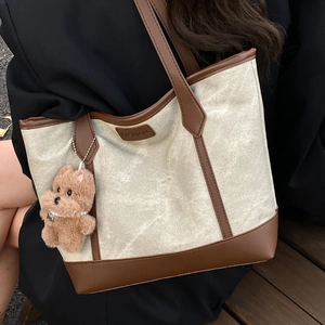 Large beige canvas tote bag with brown leather trim and teddy bear charm on model