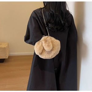 Détail d'un sac lapin en peluche avec chaîne dorée porté sur un long manteau noir