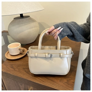 Détail d'un sac à main beige texturé avec boucle argentée sur un meuble en bois chic