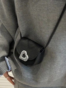 Mini black pebbled leather crossbody bag with silver heart buckle on a fashion model