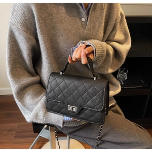 Detail of black quilted leather texture with silver metal clasp and chain strap