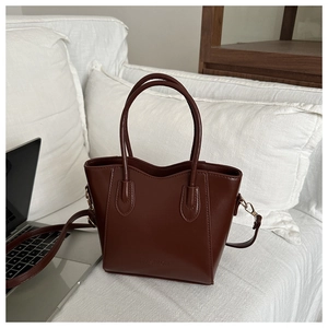 Close-up of matte dark brown bucket bag with FASHION logo on white soft bedding