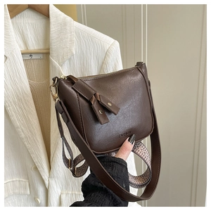 Detail van donkerbruine leren crossbodytas met dubbele riemen en modieuze reliëftekst