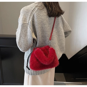 Détail d'un sac bandoulière en fausse fourrure rouge avec ferrures argentées sur tricot