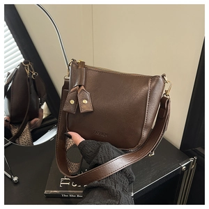 Detail van donkerbruine leren crossbodytas met FASHION-reliëf en brede schouderband