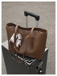 Close-up of a large brown tote bag with heart-print scarf on a silver suitcase