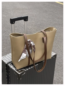 Large beige tote bag with brown straps and silk scarf detail on a metallic suitcase