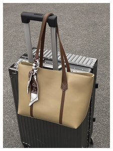 Beige leather tote bag with silk scarf hanging on a silver metal suitcase luggage handle