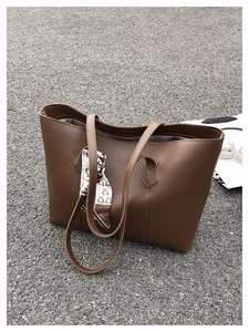 Close-up of brown leather tote bag with a decorative silk scarf on the handles