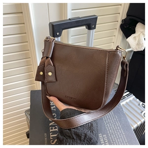 Detail van donkerbruine leren crossbodytas met reliëf FASHION-logo en brede schouderriem