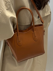Brown leather fashion tote bag with top handle and shoulder strap shown on a model