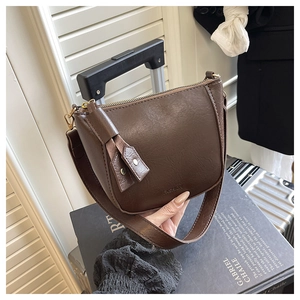 Detail van donkerbruine leren crossbodytas met brede riem en modebelettering