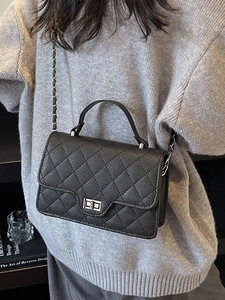 Chic black quilted crossbody bag with silver chain strap and top handle on a model
