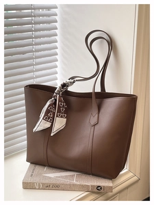 Close-up of brown leather tote bag with a decorative silk scarf on a book by the window