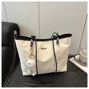 Detail of white marble pattern tote bag with black straps and plush toy charm on a desk