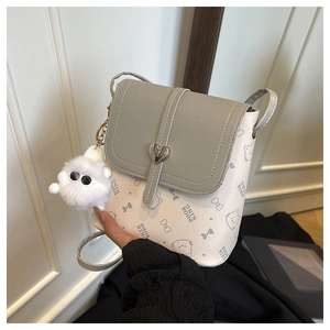 Detail of cream mini bucket bag with cat pattern, heart clasp and plush pompom charm