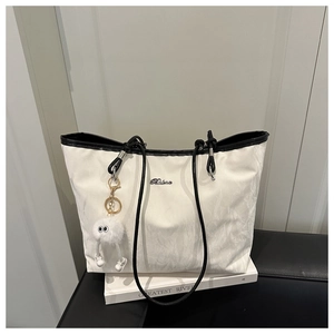 Detail of white textured tote bag with black handles and a cute plush ball charm