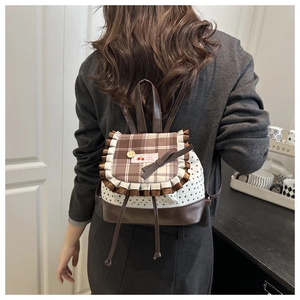 Detail of a brown plaid backpack with ruffle trim and cherry label on star printed fabric