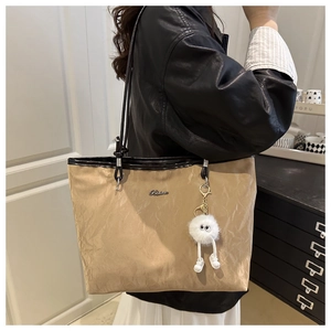 Detail of beige pleated tote bag with black straps and a quirky white fuzzy pendant