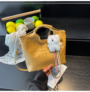 Detail of yellow woven handbag featuring a white plush bear charm and matching strap