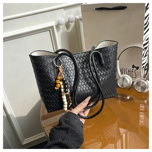 Detail of black woven pattern tote bag featuring a colorful beaded charm and slim handles