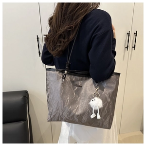 Detail of silver-grey tote bag showing metallic pleated texture and plush doll charm