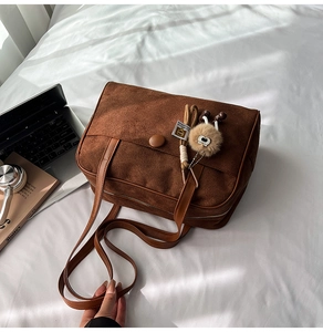 Detail view of large dark brown suede tote bag with flap closure and plush ball keychain