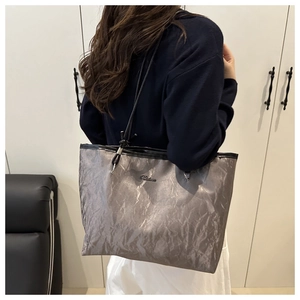 Detail view of metallic pleated tote bag showing wrinkled texture and slim shoulder straps