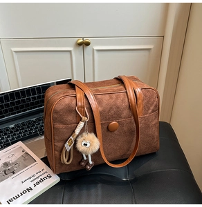 Detail of a brown suede hobo bag with large buckle pocket and plush pendant on a black seat