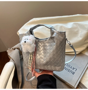 Detailed texture of silver woven tote bag with a cute white plush dog charm decoration