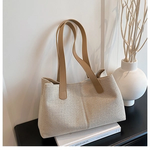 Detailed view of beige textured tote bag with brown leather straps on a modern desk