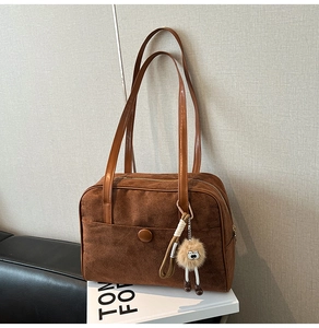 Detail of brown suede tote bag on a white display tray with a plush ball charm