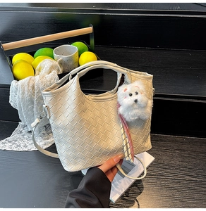Detail of cream woven leather tote bag with plush puppy charm and rainbow ribbon