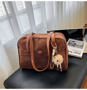 Detail of a large brown suede shoulder bag with leather handles and a plush ball charm