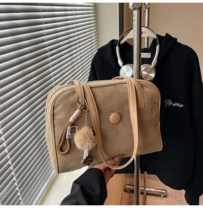 Detail of khaki suede shoulder bag featuring a fuzzy pom-pom charm and contrast stitching