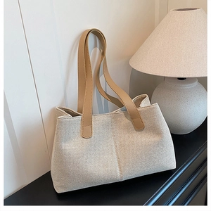 Close-up of beige canvas tote bag with brown leather handles and textured stitching