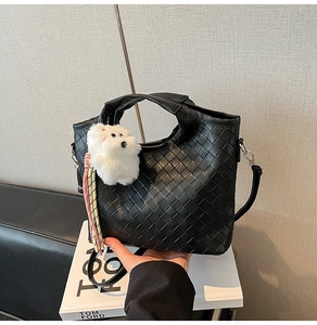 Close-up of black woven leather texture on a stylish handbag with a plush dog charm