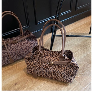 Detail view of large leopard print suede tote bags with brown handles on wooden floor