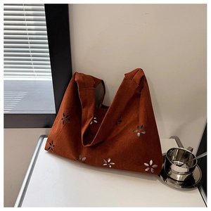 Detail of brown suede tote bag with floral laser-cut patterns on a white table