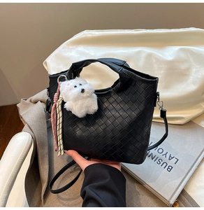 Detail of black woven leather handbag with a plush dog charm and adjustable strap