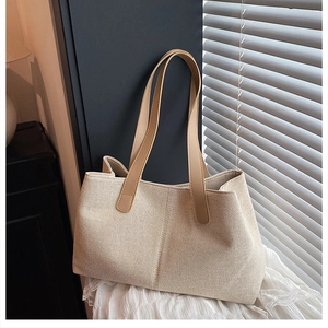 Detail of beige canvas tote bag with brown leather handles placed near window shutters