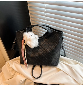 Close-up of black woven leather handbag with white plush dog pendant and tassel detail