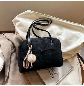Detail of black suede shoulder bag with plush charm and decorative round button