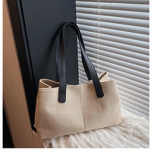 Detailed close-up of beige canvas tote bag with black leather straps on white fabric