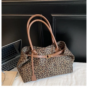 Close-up of leopard print tote bag featuring brown leather straps and gold metal buckles