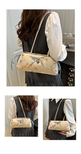 Detailed embroidery of birds and flowers on a vintage cream shoulder bag with a blue bow