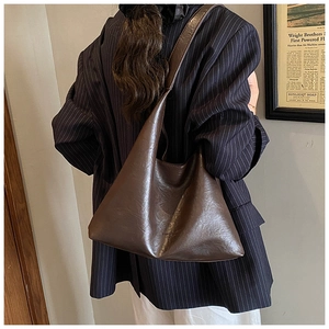 Detail of a dark brown matte leather hobo bag worn by a model in a retro indoor setting