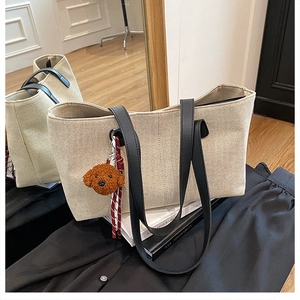 Detail of canvas tote bag with black PU straps and cute brown puppy plush charm